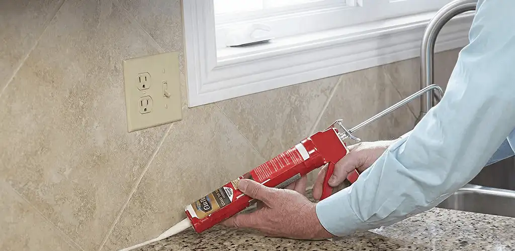 Handyman applying caulk along a kitchen backsplash and countertop seam in Sarasota, FL