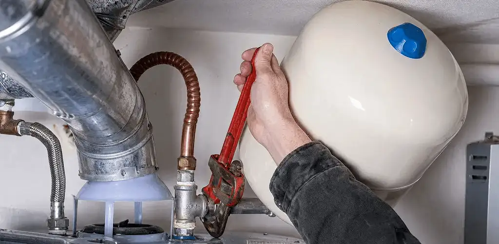 Water heater repair technician tightening plumbing connections near a tank unit in Sarasota, FL